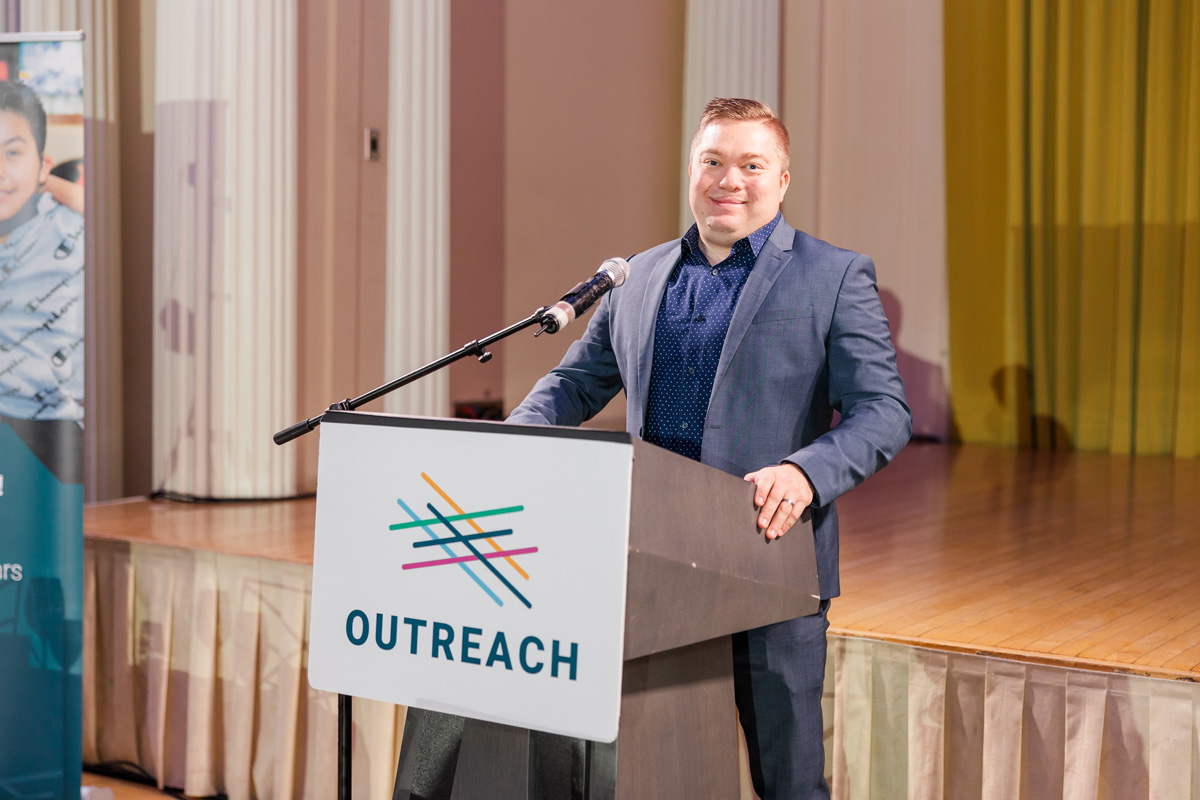 Eric C. Smith speaking at a podium bearing the Outreach logo