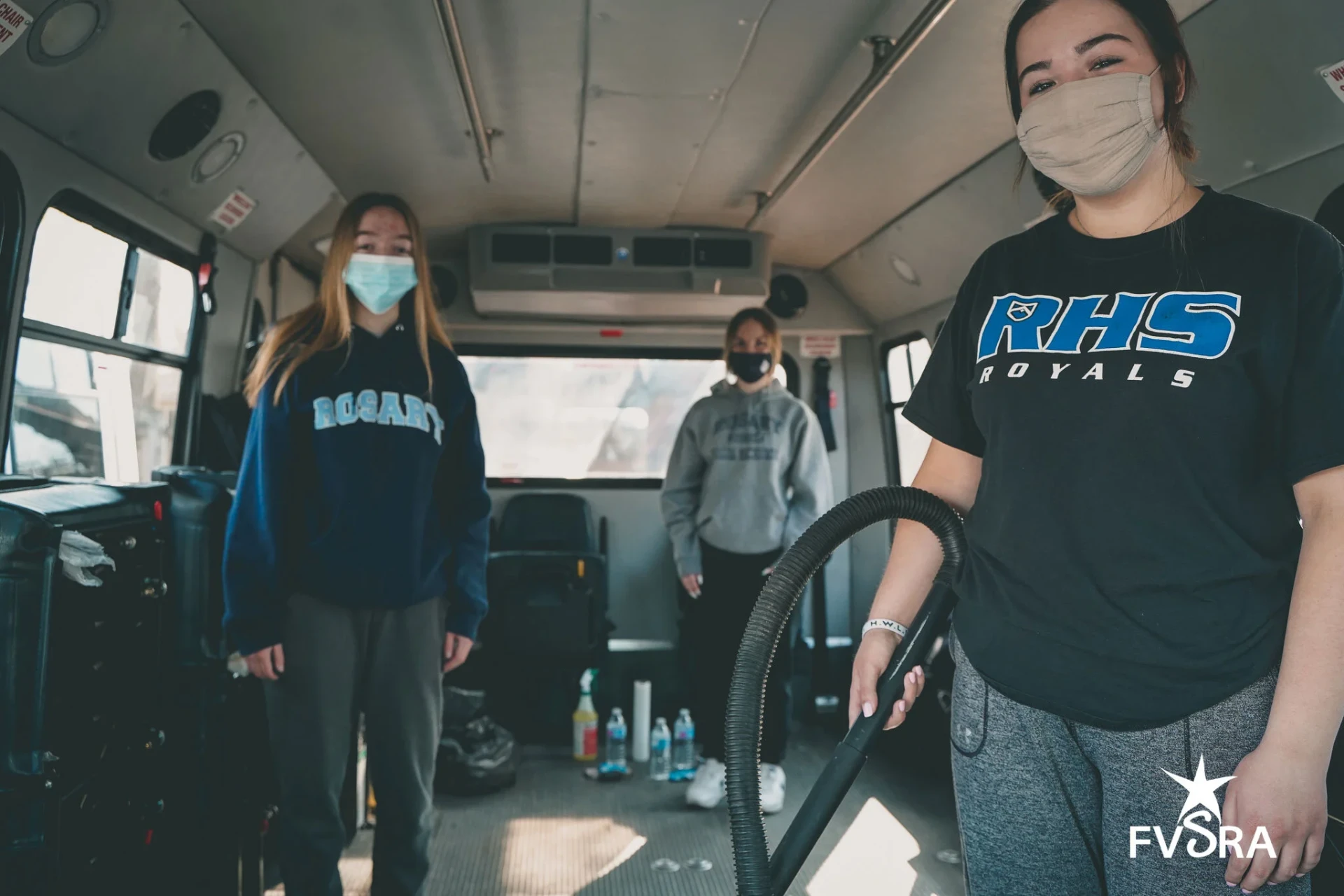 Three masked Rosary High School students cleaning the interior of an FVSRA bus