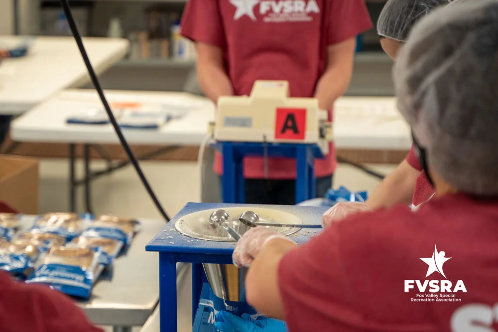 Volunteers in FVSRA shirts scooping ingredients at a packing station