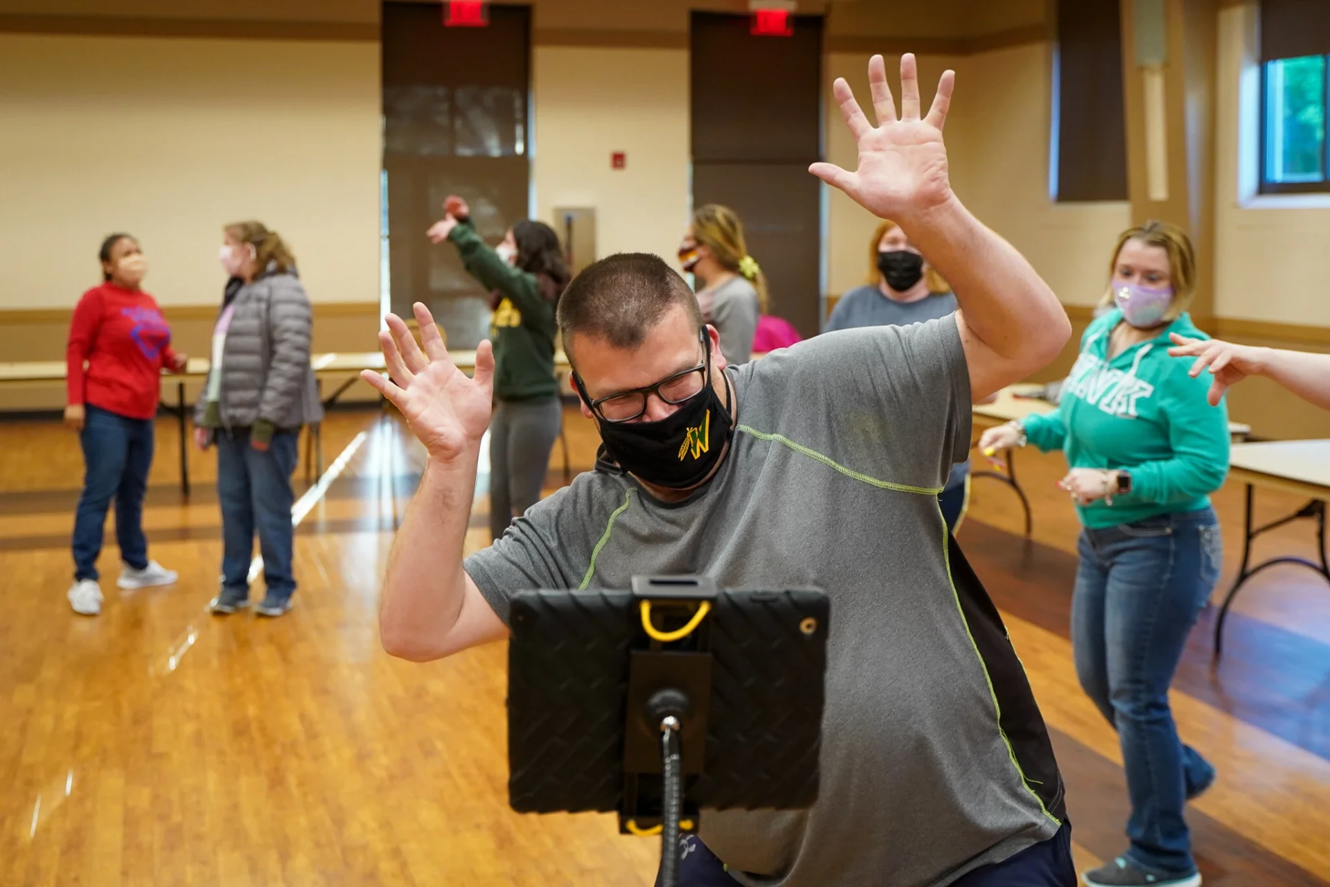 A masked participant dancing with both hands raised in front of the tablet