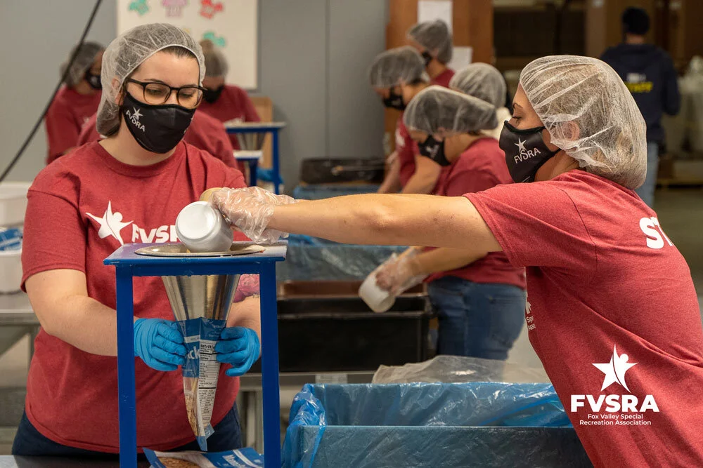 Two FVSRA staff members working together to fill meal bags at a funnel station