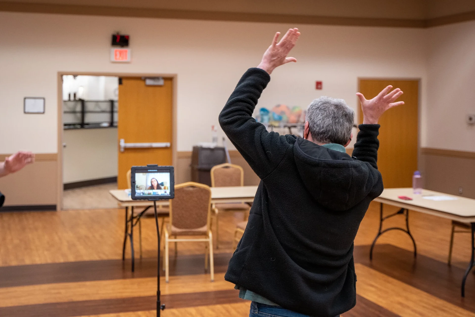 A participant seen from behind with arms raised toward the tablet screen